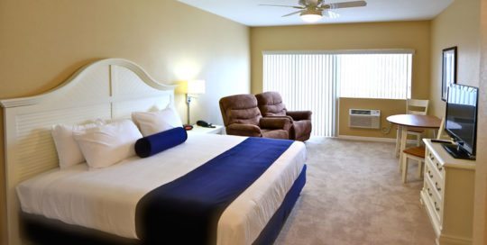 King Bed on the left wall with two recliners. Large patio doors leading to private balcony on the center wall. Dining room table with two chairs on right wall. Dresser with TV on right wall.