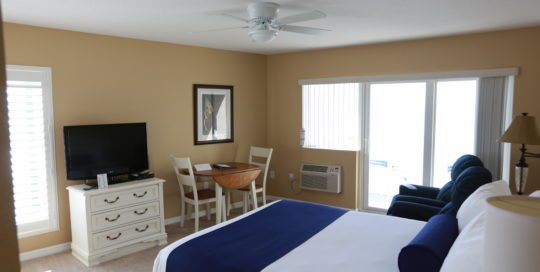 Dresser with TV on the left wall. Dining room table with two chairs on left wall. Patio doors leading to balcony on the center wall. Two recliners and one queen bed along the right wall.