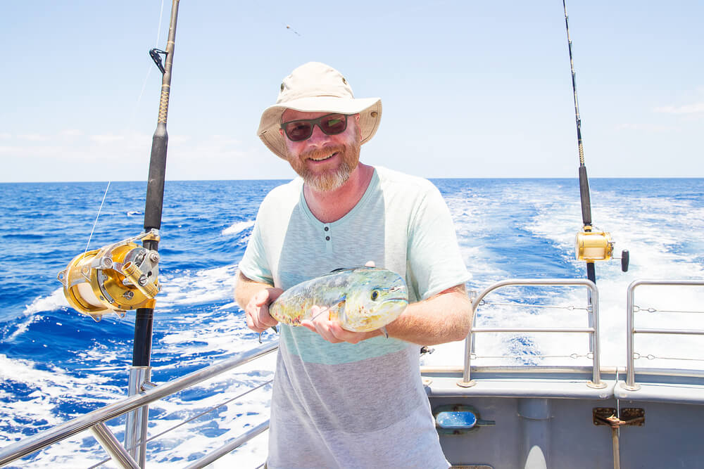 A man smiles and holds a fish, while on a fishing charter in Madeira Beach, Florida.